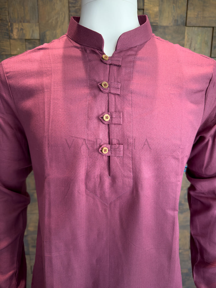 Pink kurta on a mannequin against a wooden panel background. A minimalist dusty magenta designer kurta for men, balancing modern aesthetics with traditional artisanal tailoring details and a polished silhouette.