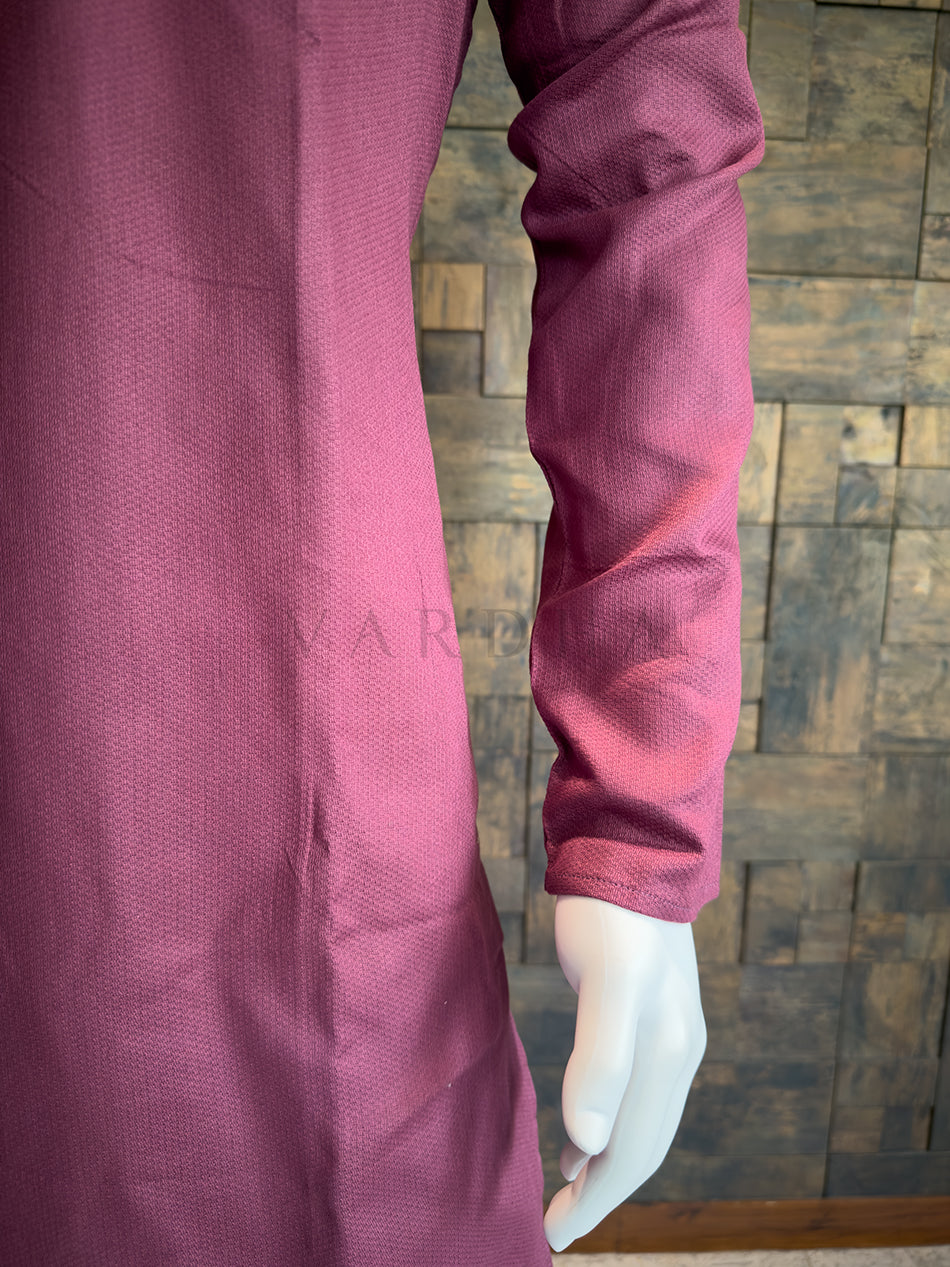 Close-up of a person wearing a maroon long-sleeve shirt against a wooden paneled wall. Versatile Mauve Pink cotton kurta with a Mandarin collar; a sophisticated ethnic piece that pairs exceptionally well with white or cream pyjamas.
