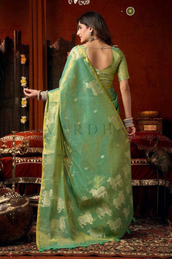 Woman in a green saree with elephant patterns in an indoor setting Back view of the radiant mint green tissue saree, emphasizing the rich golden metallic sheen, woven silver cow designs, and elegant fancy tassels.