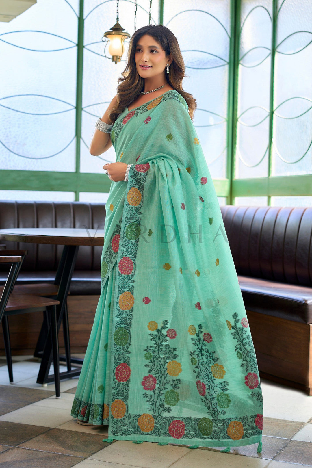Woman wearing a light green saree with floral patterns in an indoor setting. Side profile of a model draped in a mint green handloom linen saree, perfect for mehendi ceremonies and festive party-wear.