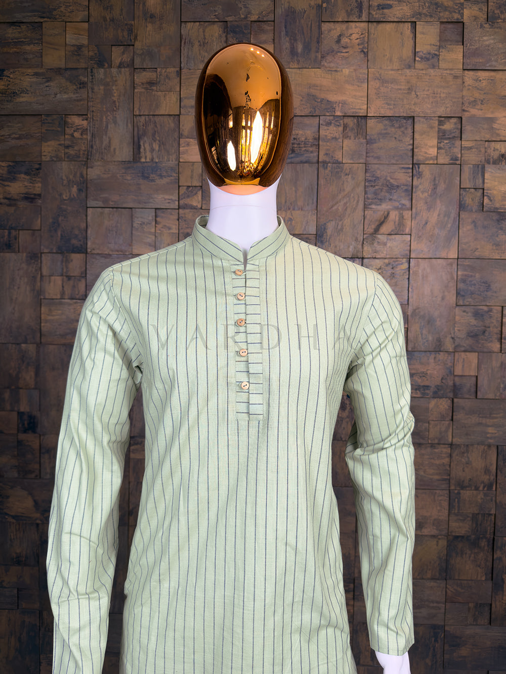Mannequin wearing a light green striped shirt against a wooden paneled wall.