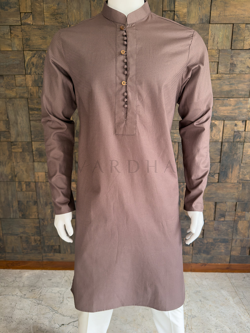 Brown kurta on a mannequin against a wooden paneled wall. Close-up of the warm taupe brown men's festive kurta showcasing the fine dobby texture and a unique center placket with alternating potli and wooden buttons.