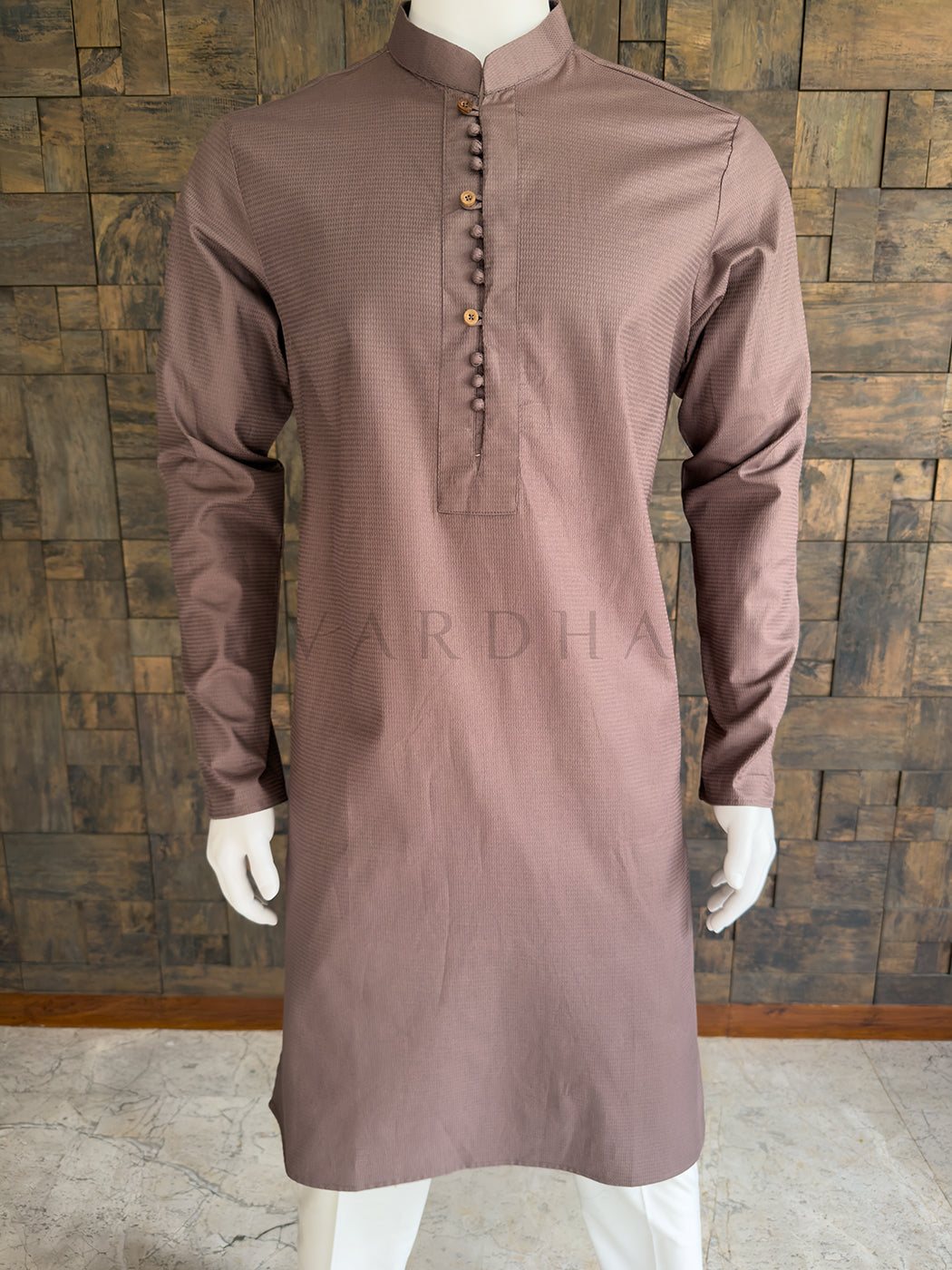 Brown kurta on a mannequin against a wooden paneled wall. Close-up of the warm taupe brown men&