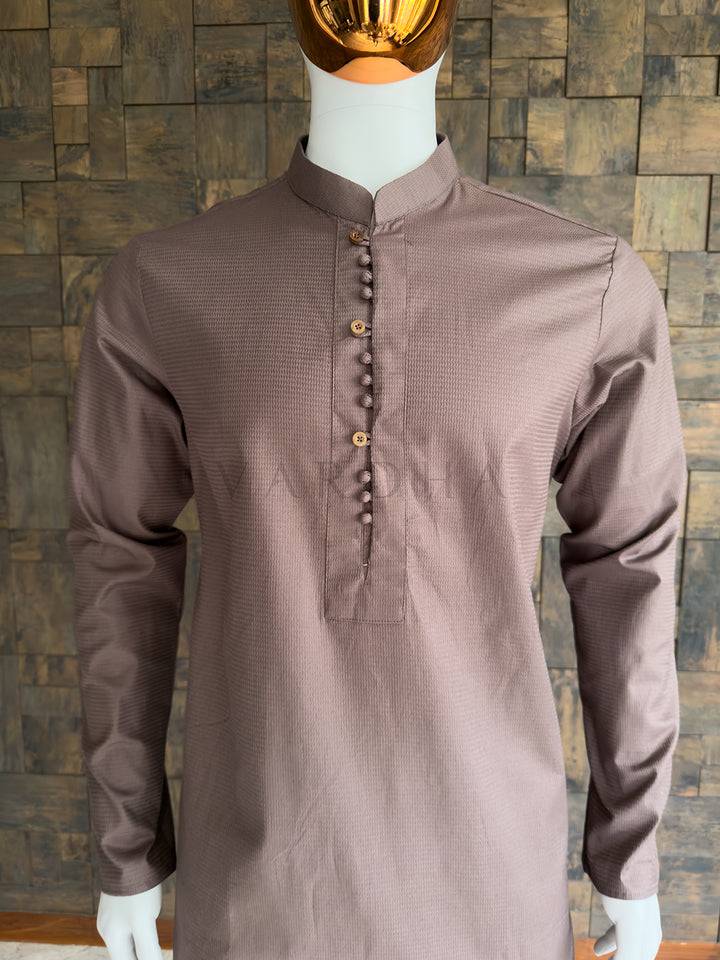 Brown kurta on a mannequin against a wooden paneled wall. Detailed chest view highlighting the crisp mandarin collar and distinctive button detailing on the premium brown textured cotton designer kurta for men.