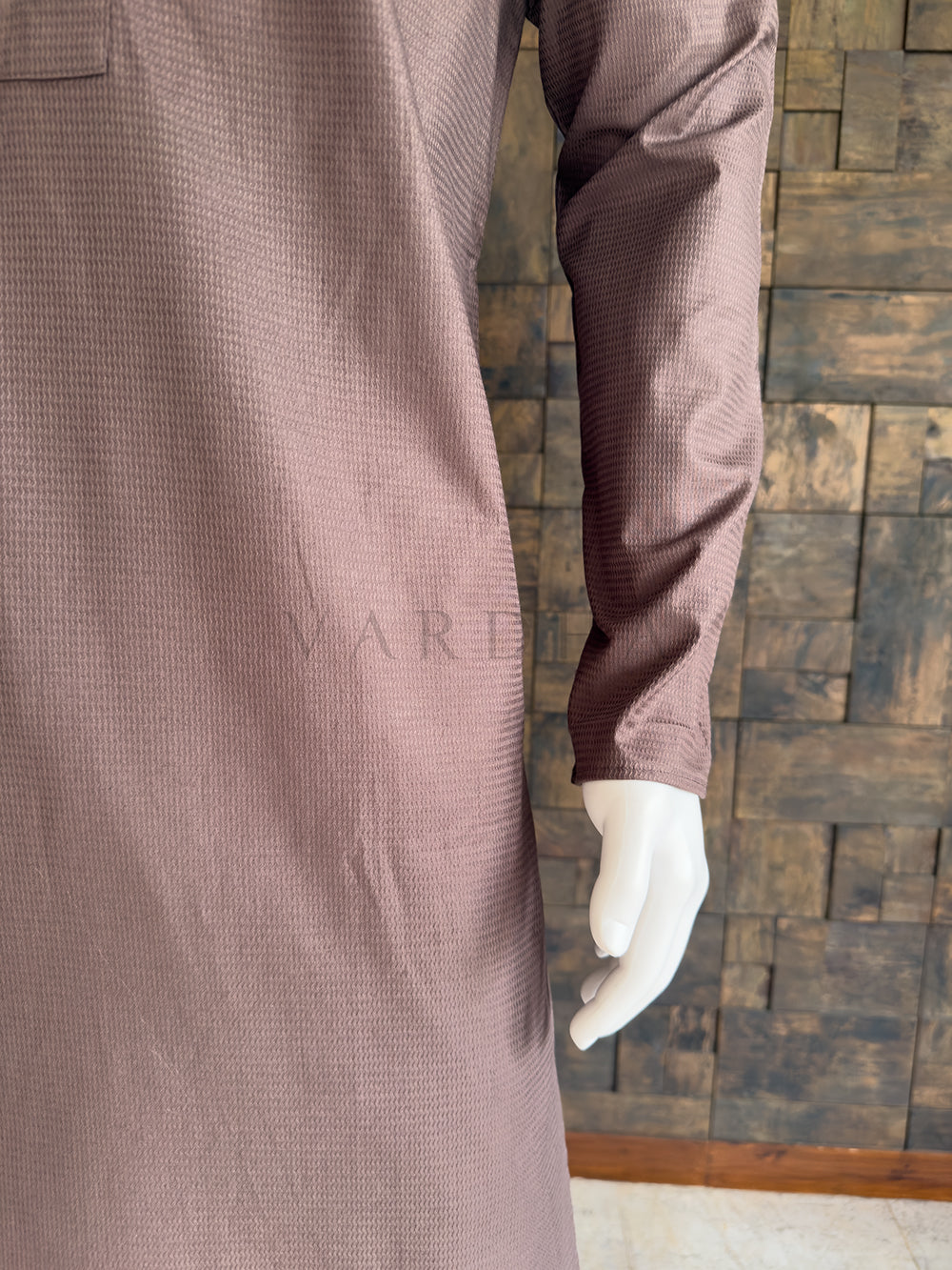 Brown textured coat on a mannequin against a wooden paneled wall. Close-up of the full sleeve and side drape of the dusty brown textured cotton kurta, showcasing the breathable premium fabric and clean, minimalist aesthetic.