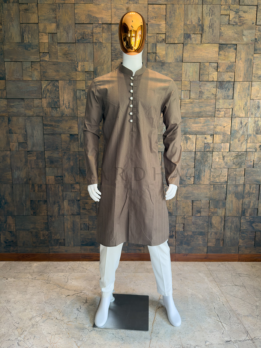 Mannequin wearing a brown kurta with a gold mask against a wooden paneled wall. Modern smart-casual ethnic wear: A knee-length Mocha Brown cotton kurta with sharp architectural lines, a Mandarin collar, and full sleeves.