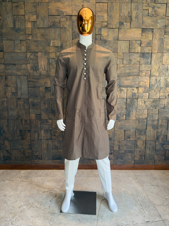 Mannequin wearing a brown kurta with a gold mask against a wooden paneled wall. Modern smart-casual ethnic wear: A knee-length Mocha Brown cotton kurta with sharp architectural lines, a Mandarin collar, and full sleeves.