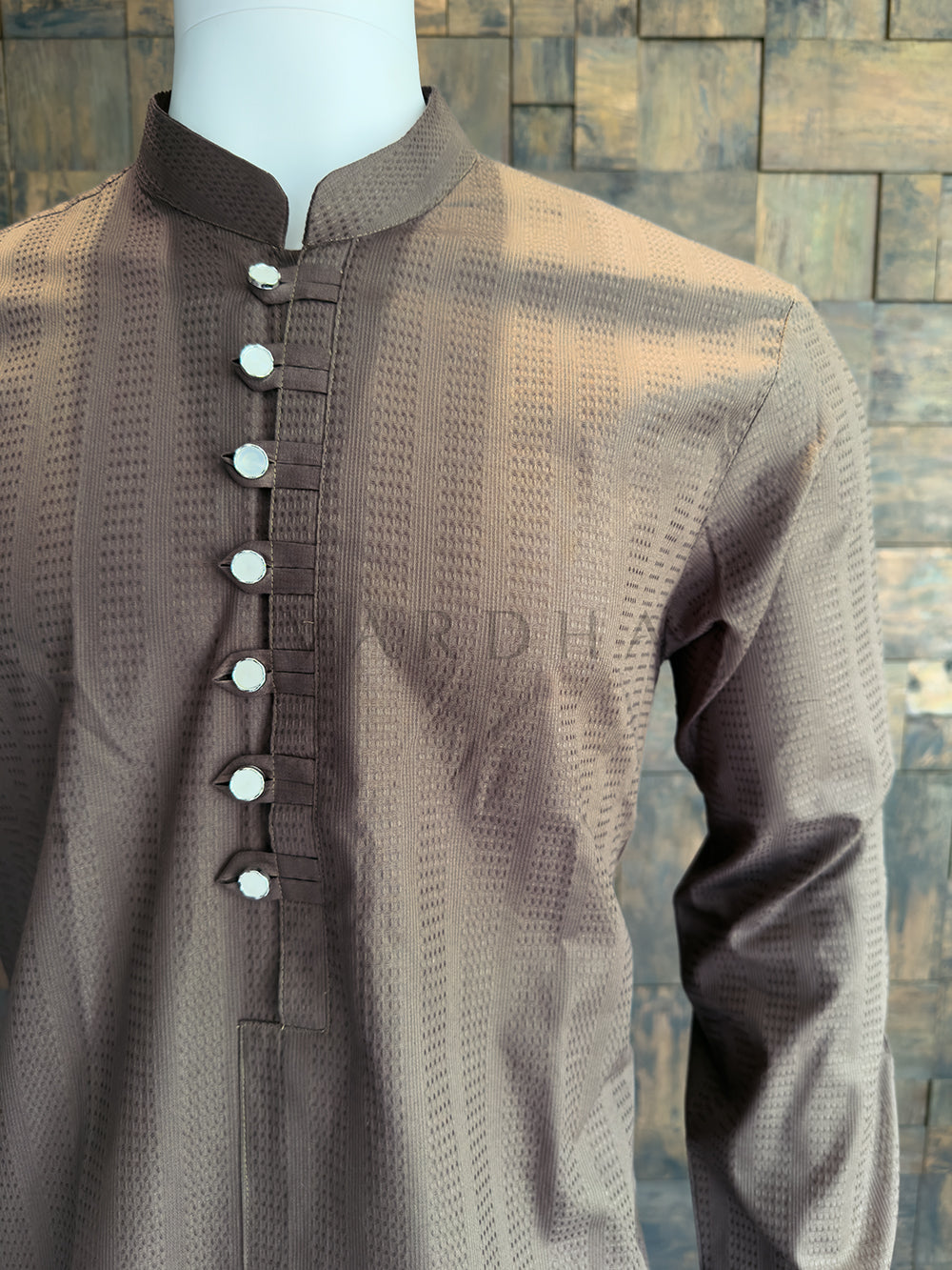 Brown textured shirt with buttons on a mannequin against a brick wall background. Refined Mocha Brown cotton kurta with a Mandarin collar; a versatile ethnic essential that pairs perfectly with white or cream pyjamas.