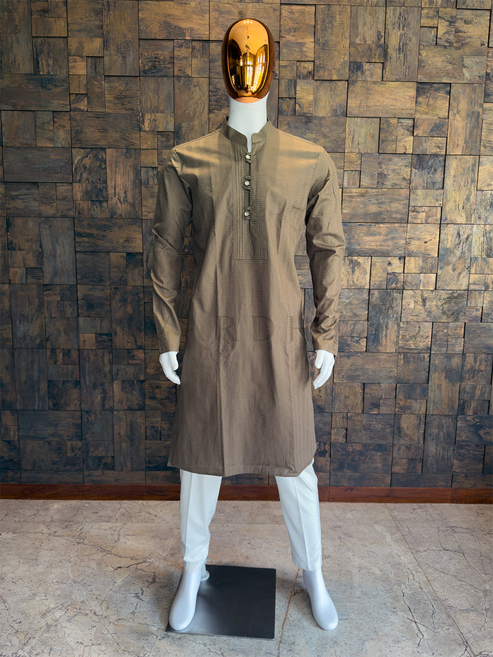 Mannequin wearing a brown long-sleeve shirt against a wooden paneled wall. This is a rich, earthy Mocha Brown long kurta. The warm, grounding tone is incredibly versatile, making it an excellent bridge piece that works perfectly for both daytime ceremonies and evening festive gatherings.