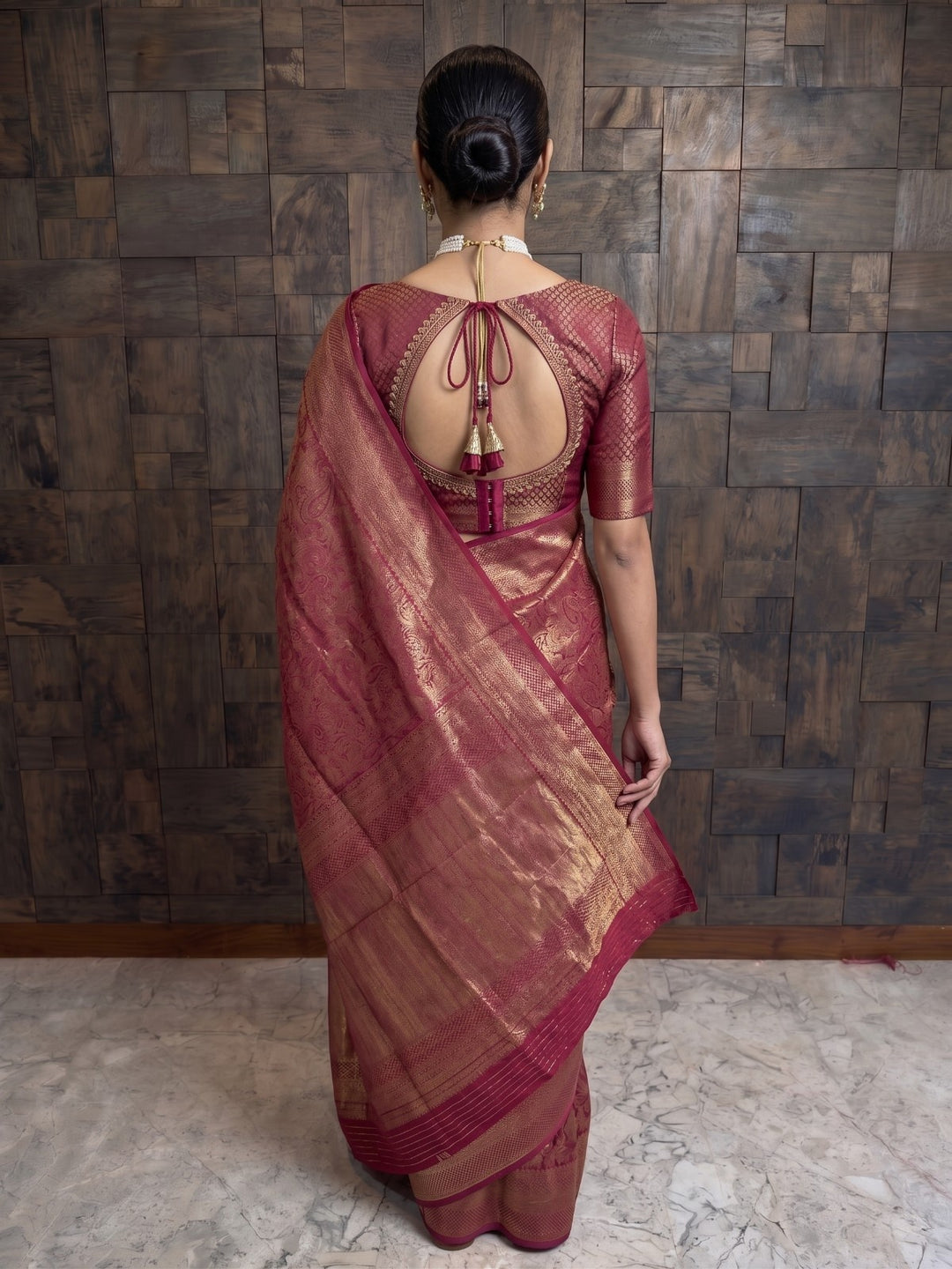 A full-length back view of a woman wearing a mulberry purple Kanjivaram silk saree. This angle highlights the matching blouse&