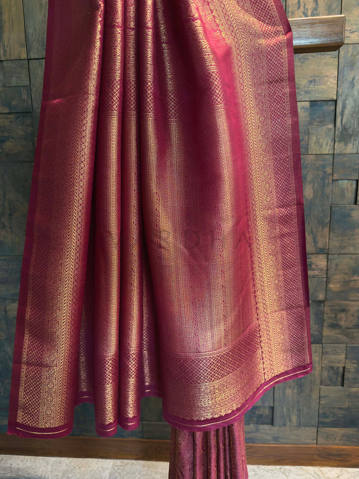 Maroon saree with gold zari patterns draped over a wooden surface against a stone wall background