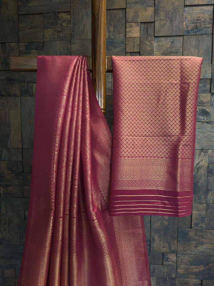 Pink fabric with intricate patterns draped over a wooden frame against a stone wall. Close-up of the traditional gold zari border framing the magenta saree.