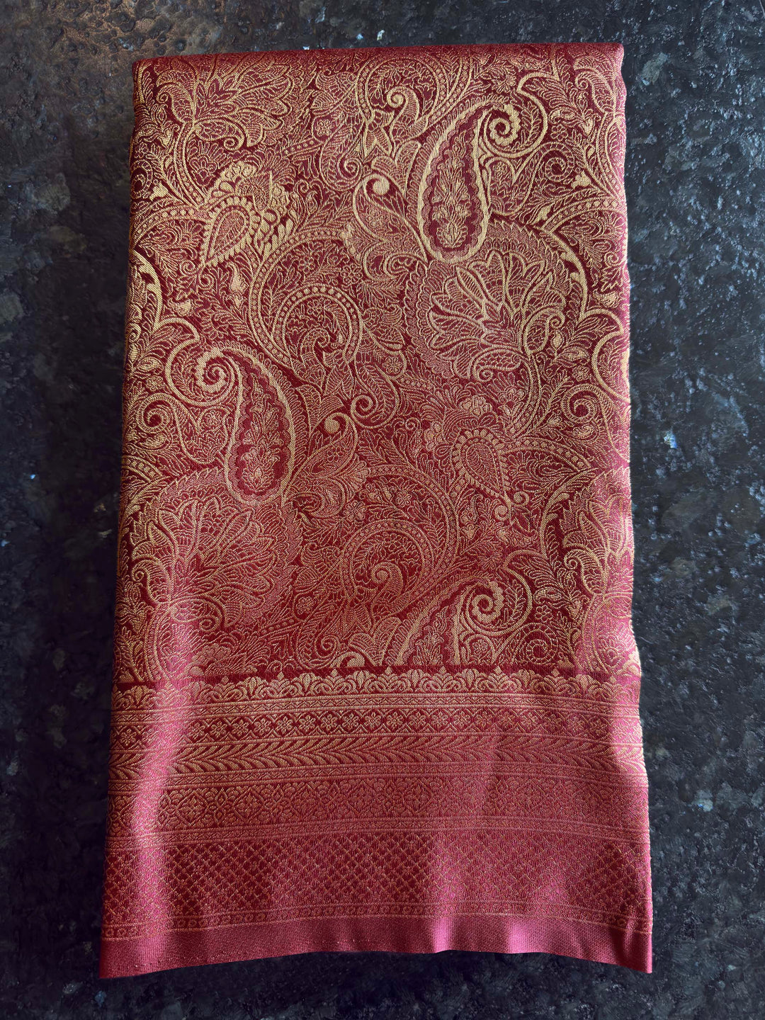 Folded view of the saree showing the heavy paisley zari pallu design. Texture shot showing the glossy sheen and smooth finish of the soft silk fabric.