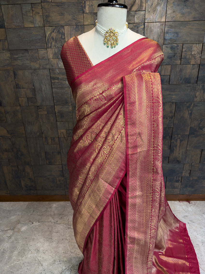 Close-up of House of Vardha red festive saree highlighting detailed gold woven traditional patterns and pallu. Magenta saree with gold patterns on a mannequin against a wooden paneled wall.