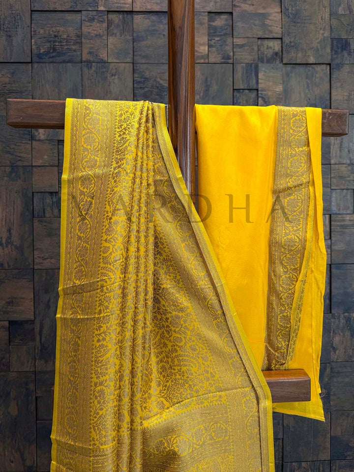 Yellow saree with intricate patterns draped over a wooden rod against a textured wall. Pleats captured to show texture fall and refined golden motif arrangement