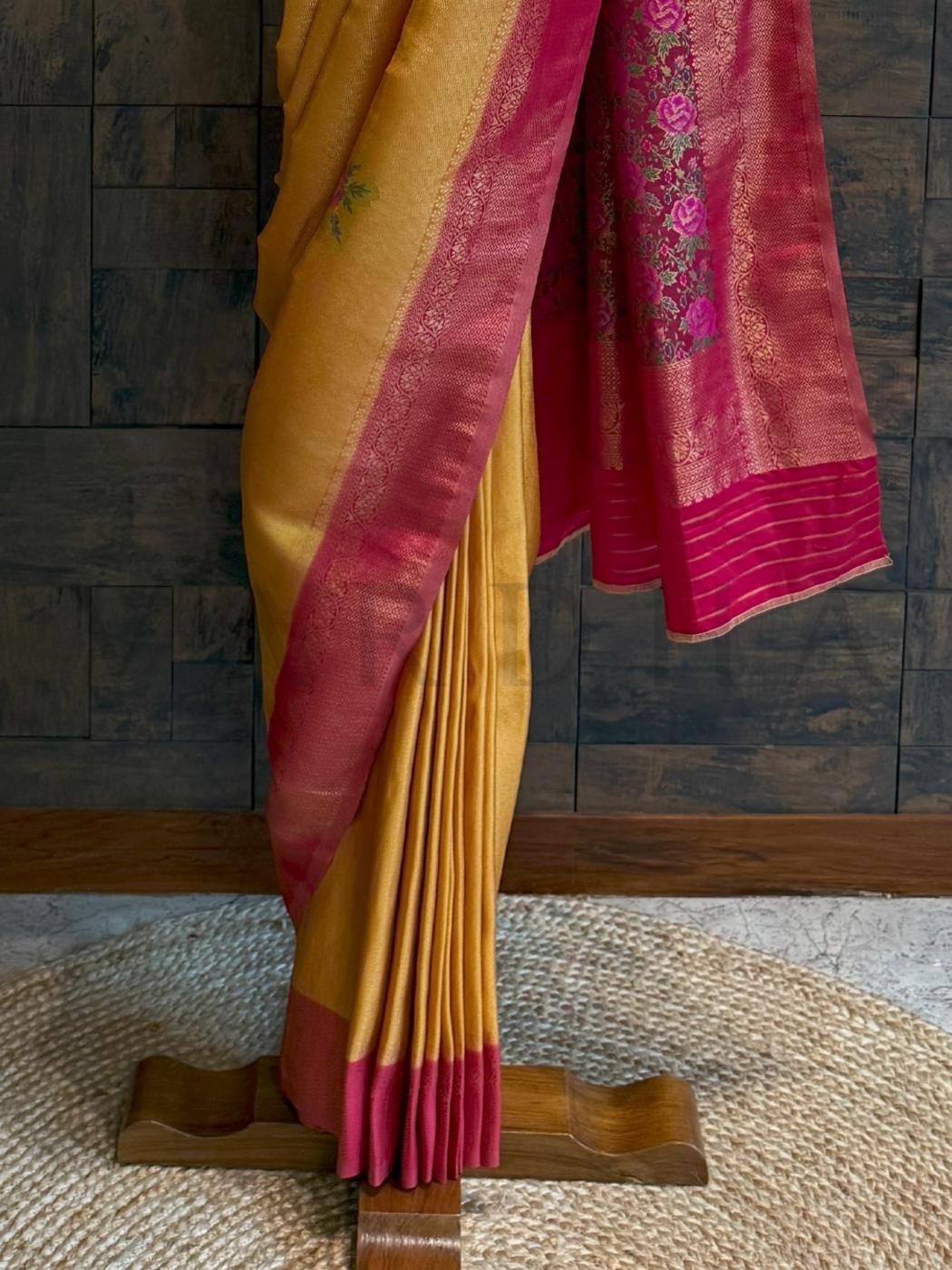 Full saree view on hanger with pallu fall in floral artistry and mustard gold body in luminous fabric., Soft art silk fabric in mustard tone paired with vibrant rani pink floral woven pallu for haldi or pooja

