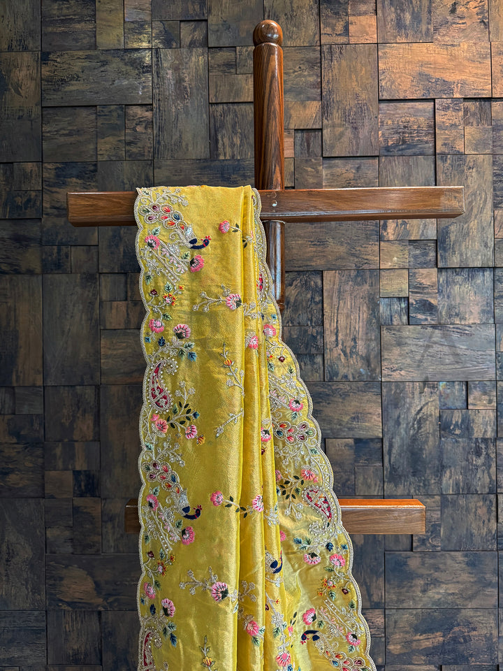 Close-up of mustard tissue saree featuring multi-color floral and bird embroidery with sequins and zari highlights.