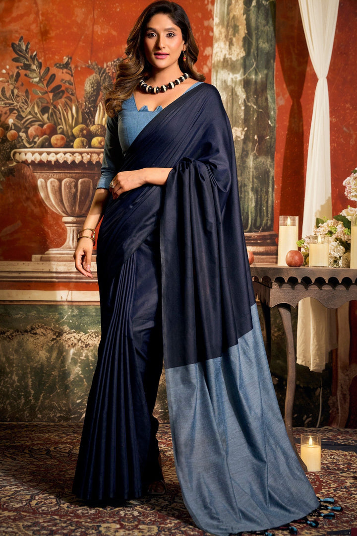Woman wearing a blue saree with a matching blouse in an elegant indoor setting. Full front view of a woman wearing a sophisticated navy blue mal cotton saree featuring a powder blue contrast pallu and fancy tassels. Beautiful woman posing gracefully in a soft navy blue mal cotton saree, showcasing the light blue contrast blouse, perfect for office wear.