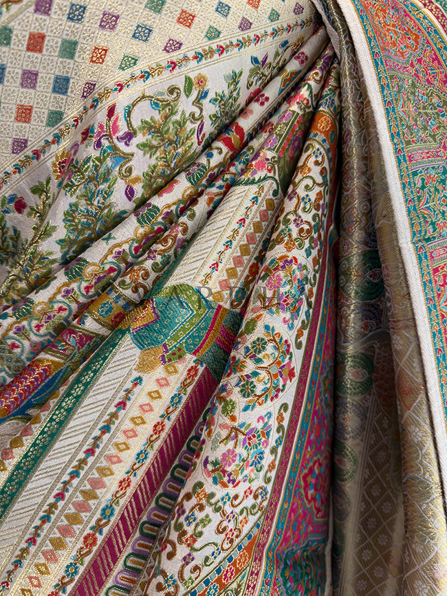 Close-up of intricately patterned fabric with a mix of floral and geometric designs. Macro texture shot of a premium off-white Meenakari silk saree in gathered pleats, revealing the highly detailed multi-colored woven diamond lattice, rich floral vines, and exquisite heritage threadwork techniques.