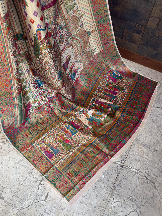 Colorful patterned fabric draped over a surface with a stone floor background Trailing edge of a luxurious cream festive Meenakari saree displayed on a stone floor, revealing an elaborate pallu heavily woven with detailed royal court figures, elephant motifs, and vibrant multi-colored traditional borders.