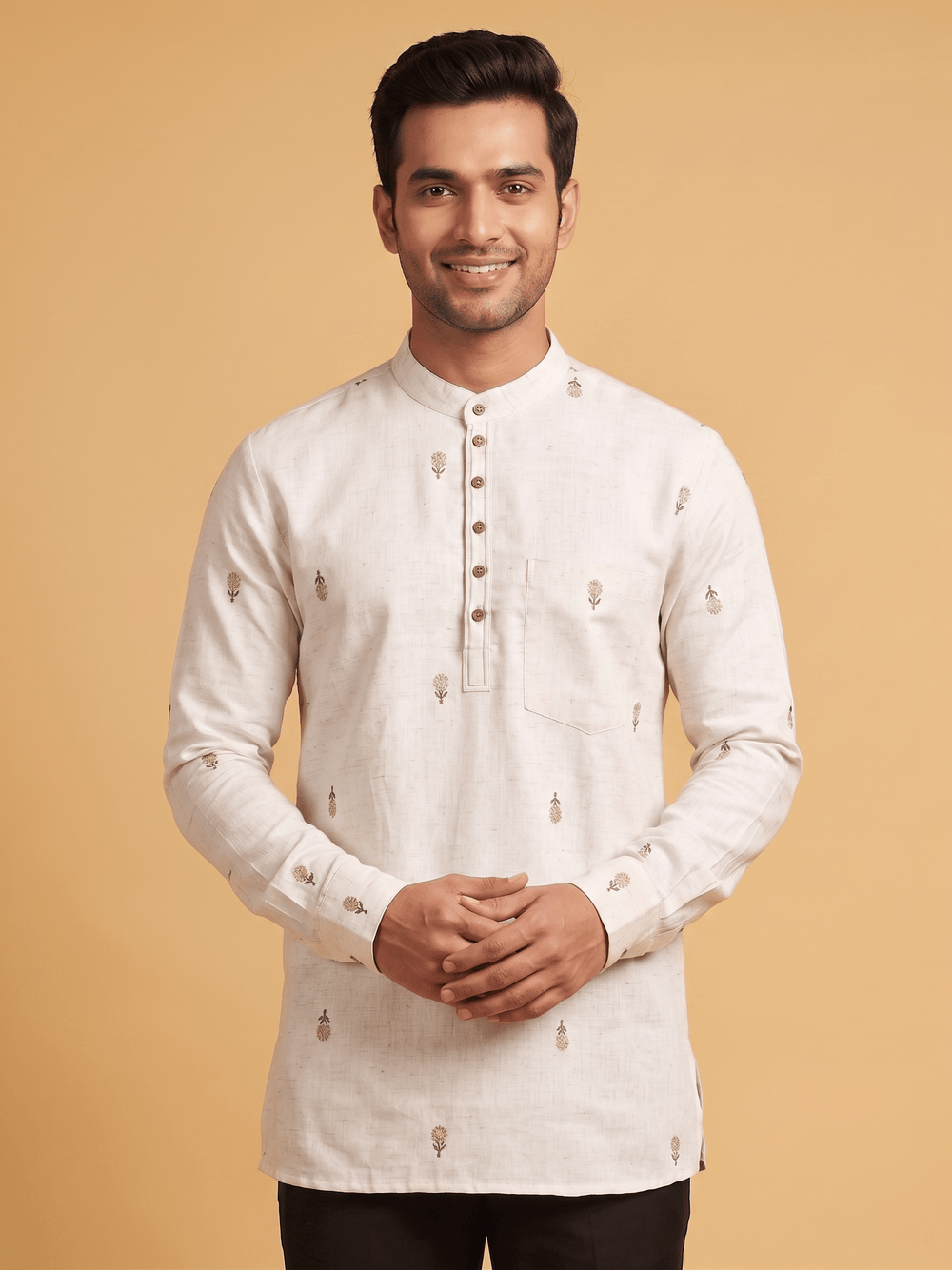 A man wearing a light beige long-sleeve kurta with small embroidered motifs, standing against a solid warm beige background. Close-up of the mandarin collar and subtle floral embroidery on an off-white cotton short kurta.