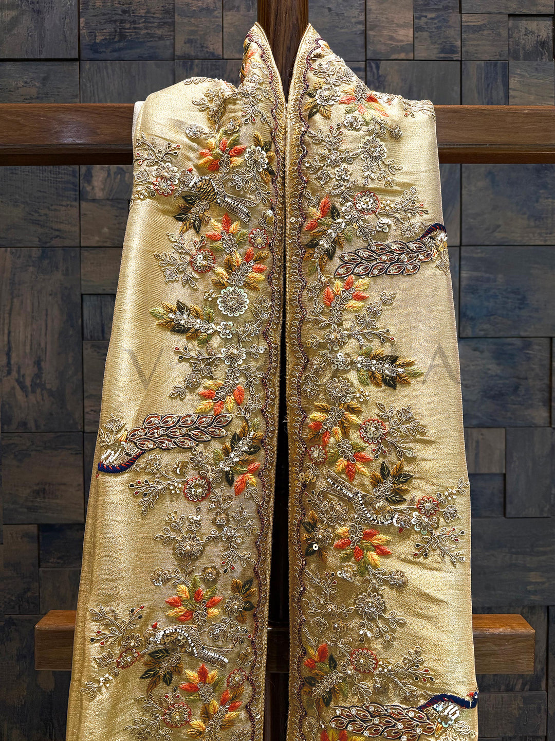 Slight Flat lay of the saree displaying full embroidery panel with floral vines and regal patterns. Decorative robe with floral and paisley patterns on a wooden surface