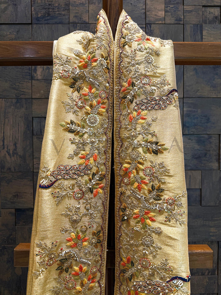 Slight Flat lay of the saree displaying full embroidery panel with floral vines and regal patterns. Decorative robe with floral and paisley patterns on a wooden surface
