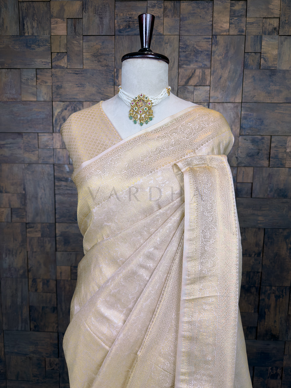 Beige saree on a mannequin against a textured wall background. Lustrous Off White Kanjivaram Silk Saree by House of Vardha showcasing a dense and ornate traditional Gold Zari Weave border and pallu. House of Vardha Off White Kanjivaram Silk Saree featuring an intricate Gold Zari Weave with traditional motifs, elegantly draped on a mannequin. We offer Ready to wear, Pre drape service, Saree Add on, Custom Stitched Blouse, Fall and Edging, Gift Packaging at Complimentary Price!