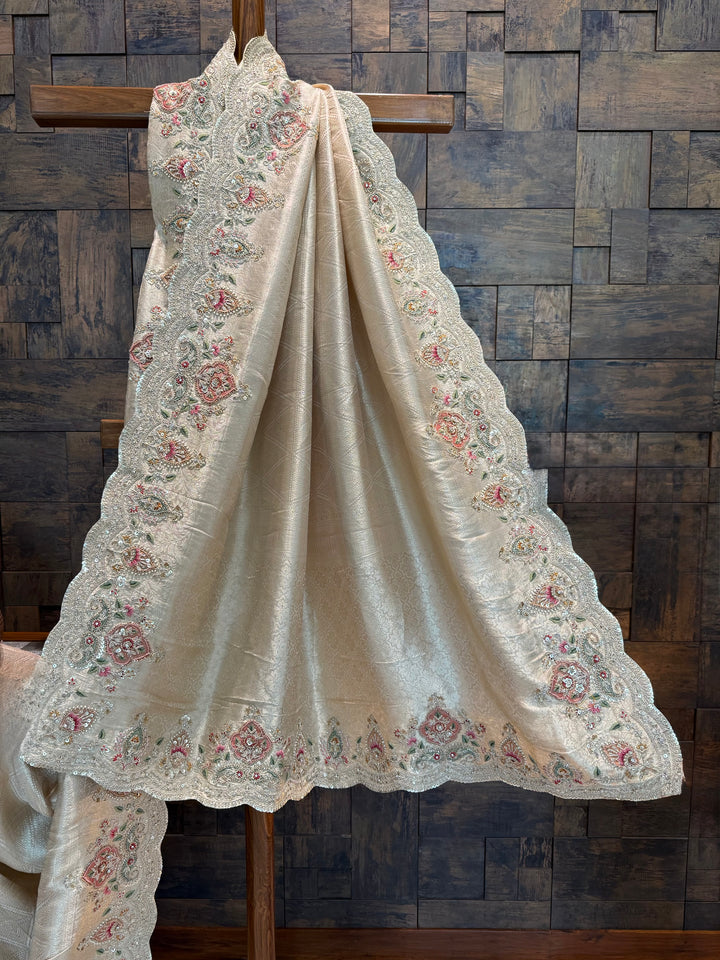 White embroidered fabric draped over a wooden cross against a wooden paneled wall. Scalloped edge of Kanjivaram tissue silk saree showing rich zari and embroidery craftsmanship

