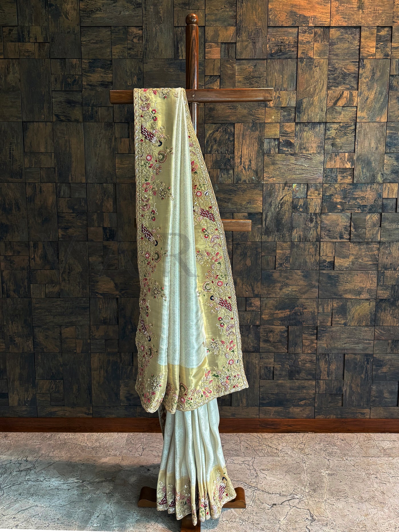 Off White Kanjivaram Tissue Saree with embroidered peacock motifs and floral zari highlights displayed on a wooden stand.