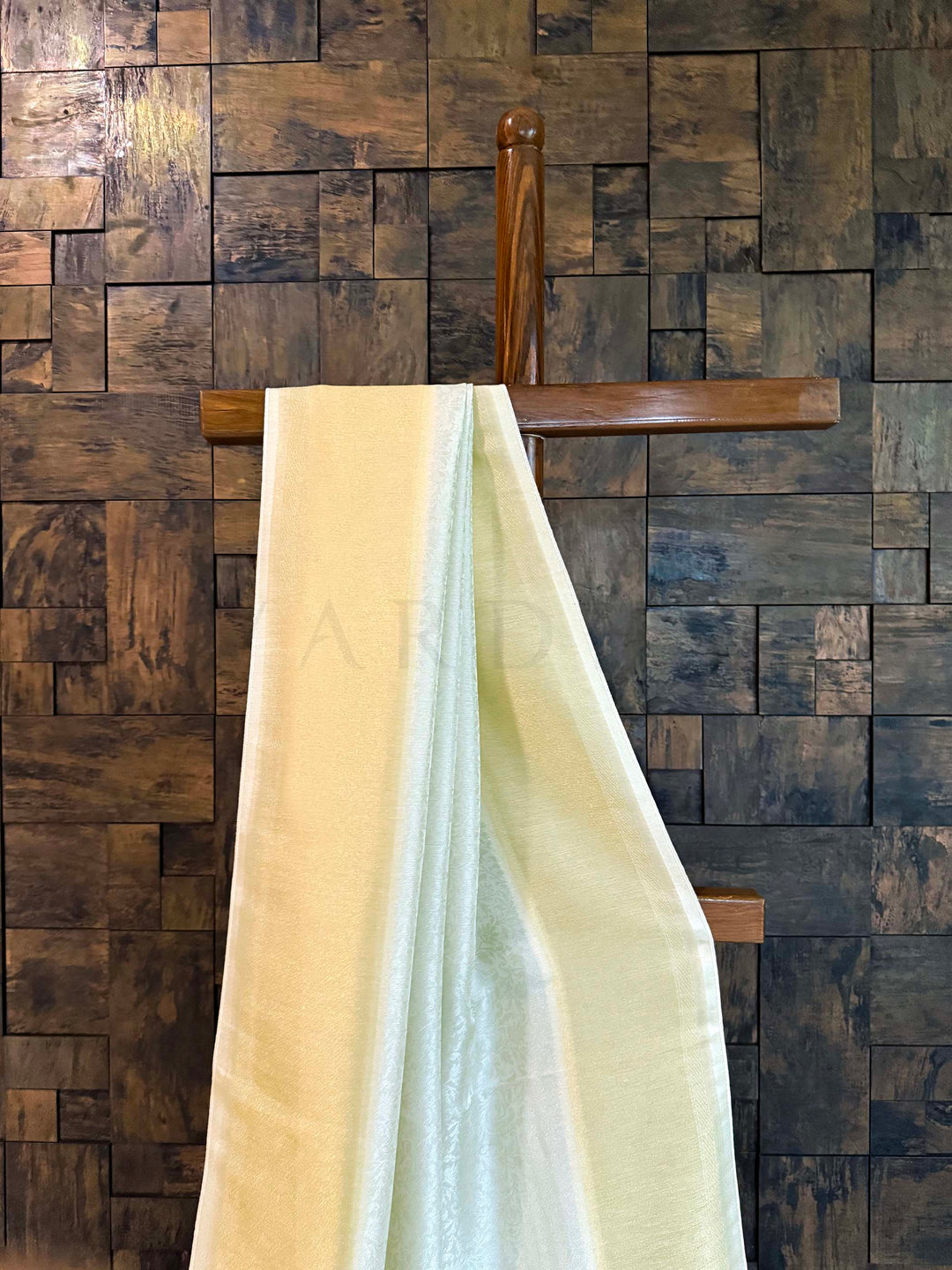 Wooden wall paneling with a draped fabric in front Pleats of pistachio-mint saree with gold border emphasizing fluid fall.