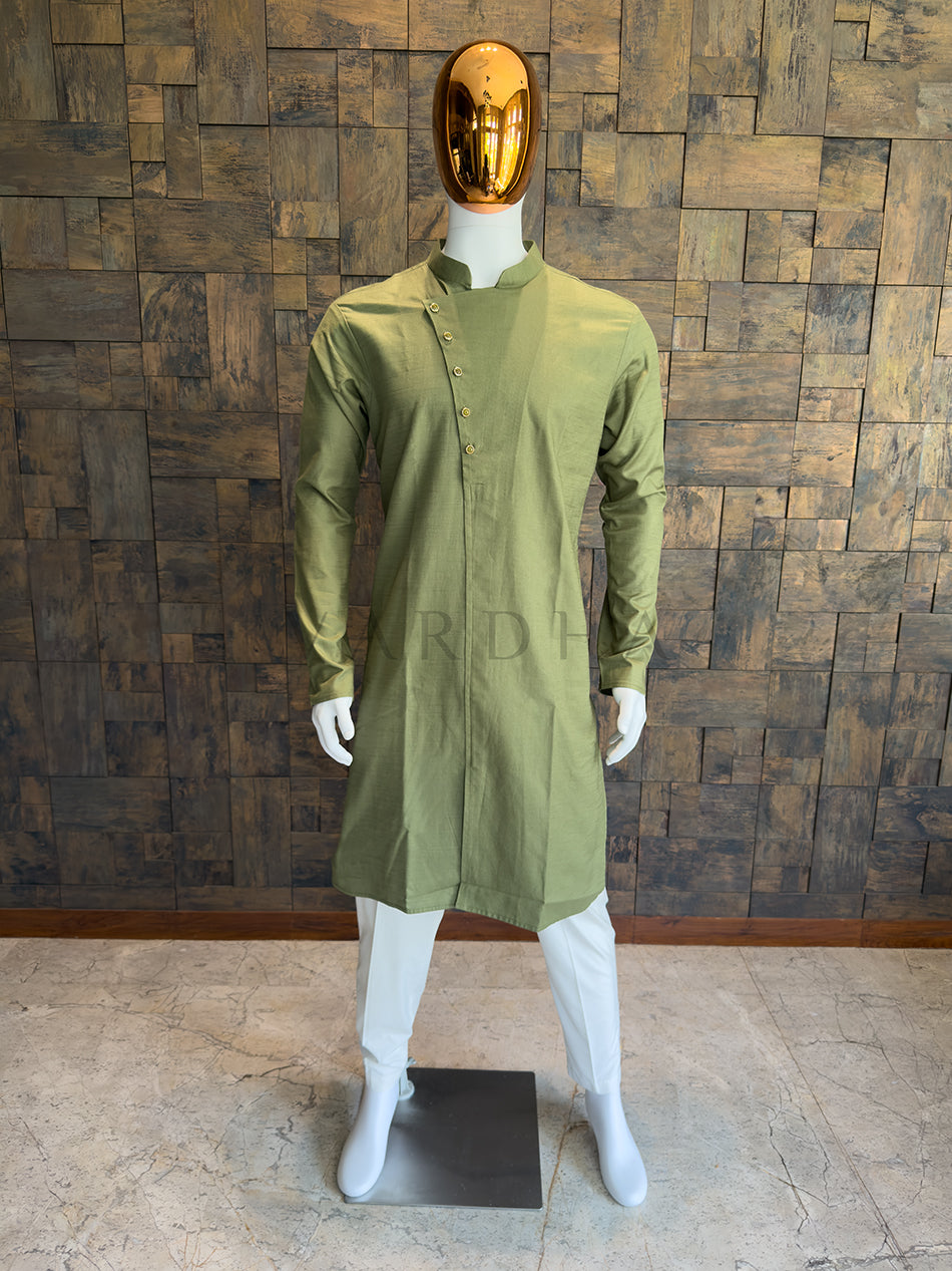 Mannequin wearing a green kurta with white pants against a wooden paneled wall. Front view of a man wearing an olive green asymmetrical cotton kurta with an angled button placket.