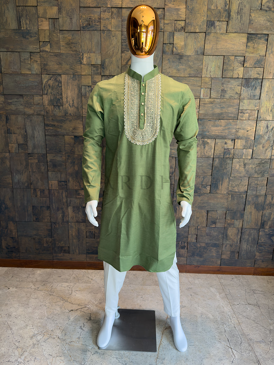 Green kurta with intricate neckline on a mannequin against a wooden paneled wall. A regal Olive Green knee-length kurta with heavy traditional ornamentation and a subtle festive sheen, designed for grand weddings and sangeet nights.