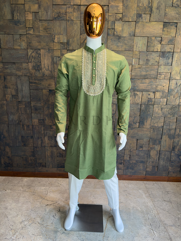 Green kurta with intricate neckline on a mannequin against a wooden paneled wall. A regal Olive Green knee-length kurta with heavy traditional ornamentation and a subtle festive sheen, designed for grand weddings and sangeet nights.