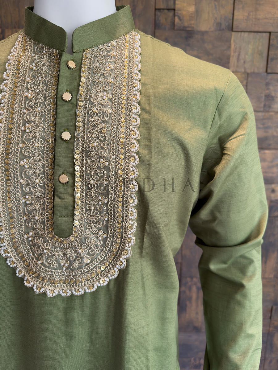 Green kurta with intricate gold embroidery on a wooden background. An elegant Olive Green kurta for the groom’s squad, featuring shimmering sequins and Zari work, ideal for mehendi ceremonies and festive celebrations.
