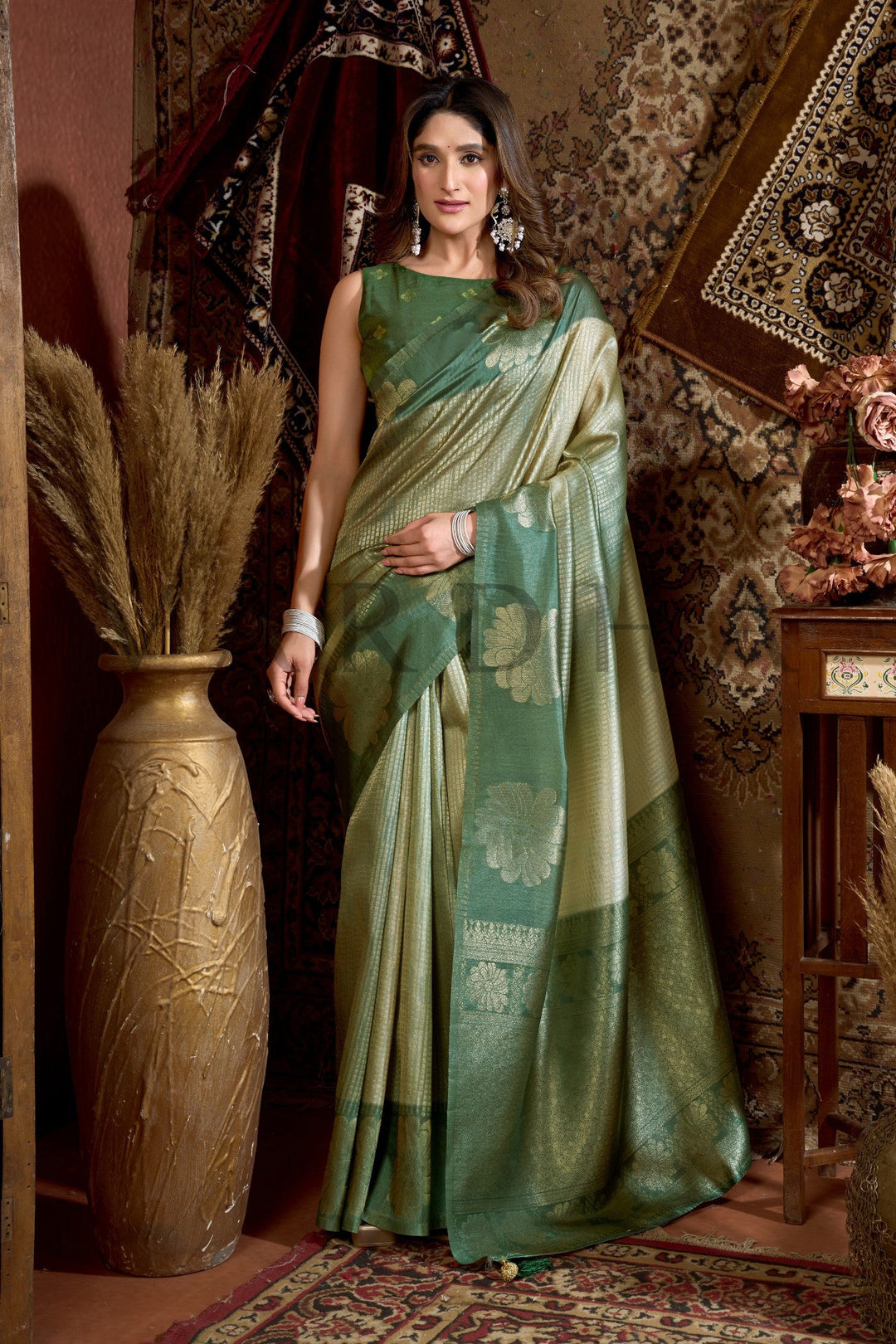 Woman in a green saree standing in an ornate room with decorative elements. Front view of a model wearing an elegant Olive Green and Golden Beige Prijam Kota Silk Saree with floral zari work.