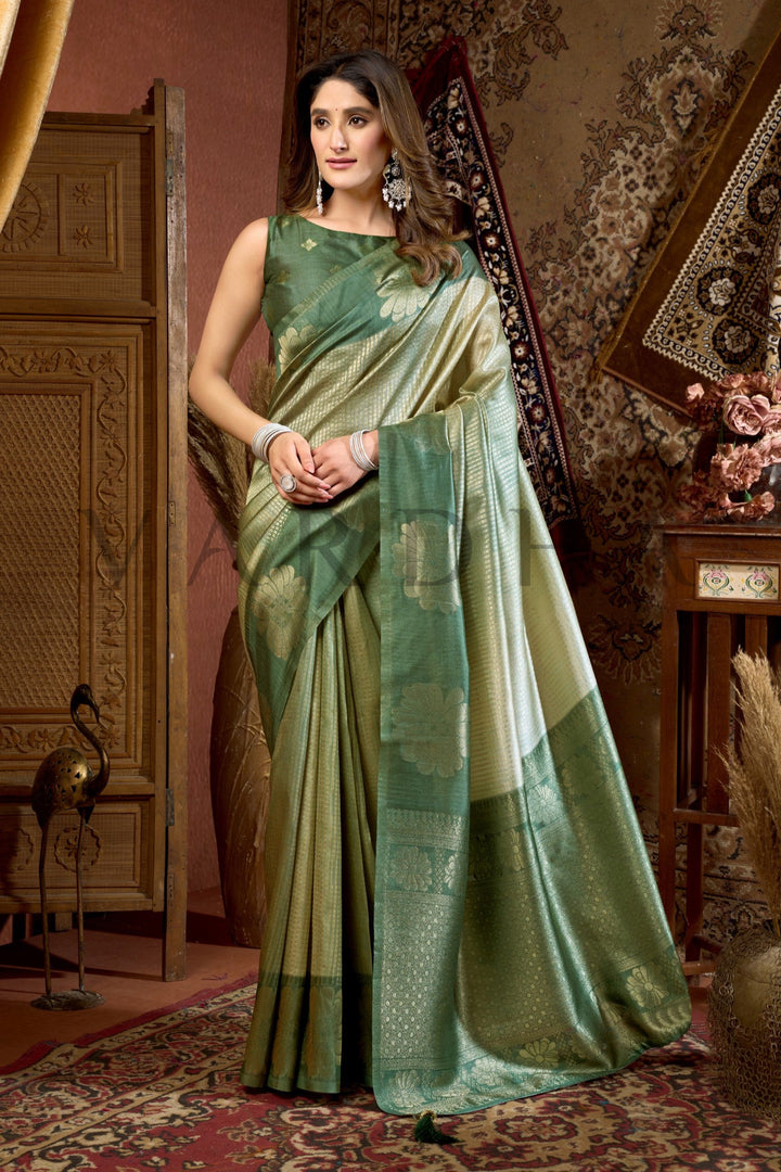 Woman in a green saree standing in an ornate room with decorative elements. Full-length shot of a woman gracefully draping the lightweight metallic Olive Green Prijam Kota Silk Saree for festive wear.