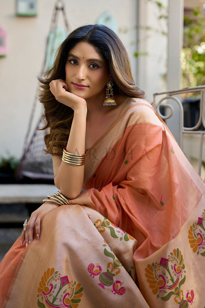 Woman in a peach saree with floral patterns sitting outdoors. Beautiful model sitting gracefully, showcasing the perfect drape, delicate body motifs, and warm peach hue of the cotton jacquard festive saree.