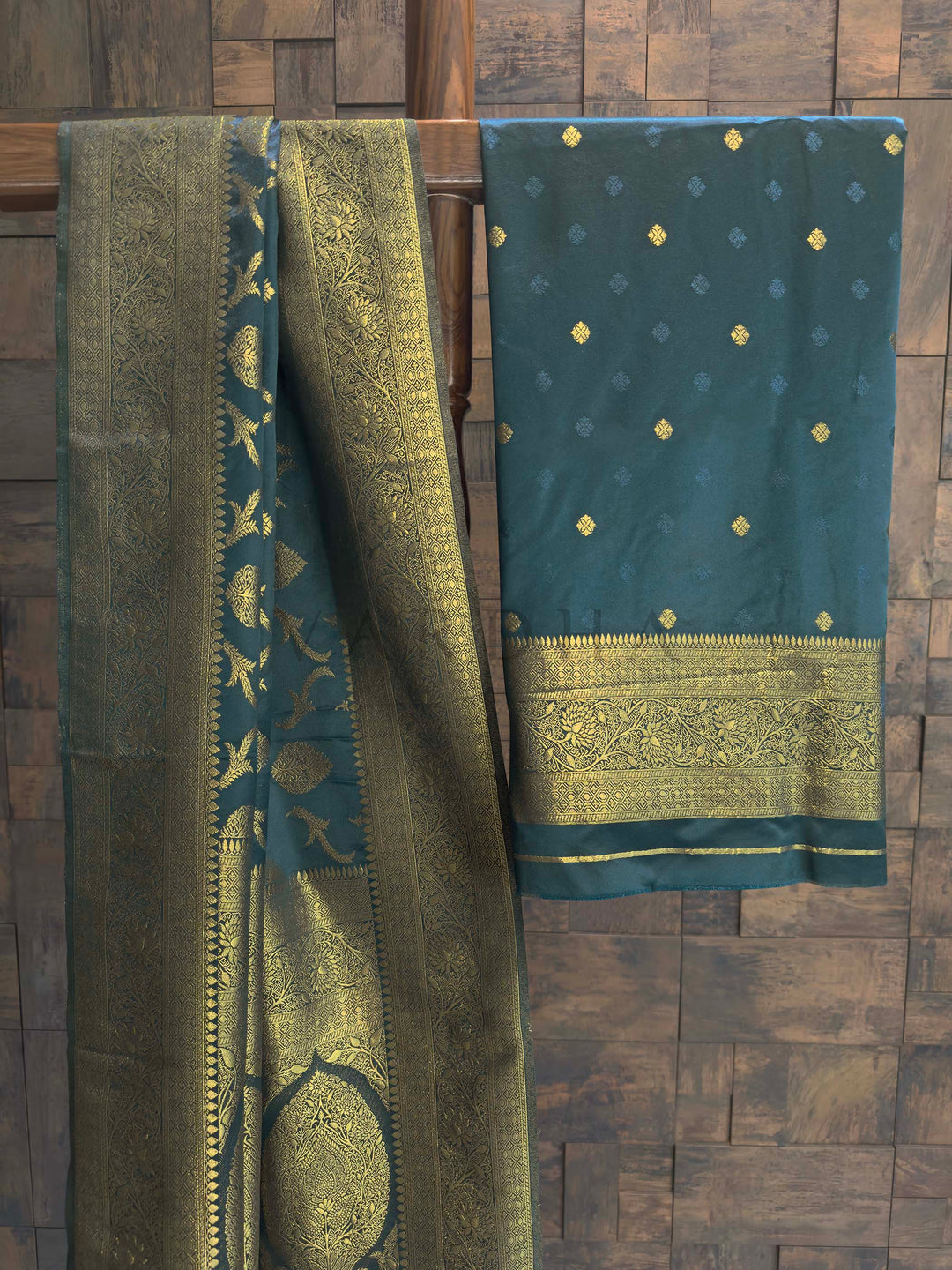 Peacock Blue Golden Zari Banarasi Satin Silk Saree House of Vardha. Exclusive House of Vardha Peacock Blue Golden Zari Banarasi Satin Silk Saree displaying an elaborate golden zari pallu and delicate motifs against a textured wall backdrop. We offer Ready to wear, Pre drape service, Saree Add on, Custom Stitched Blouse, Fall and Edging, Gift Packaging at Complimentary Price!