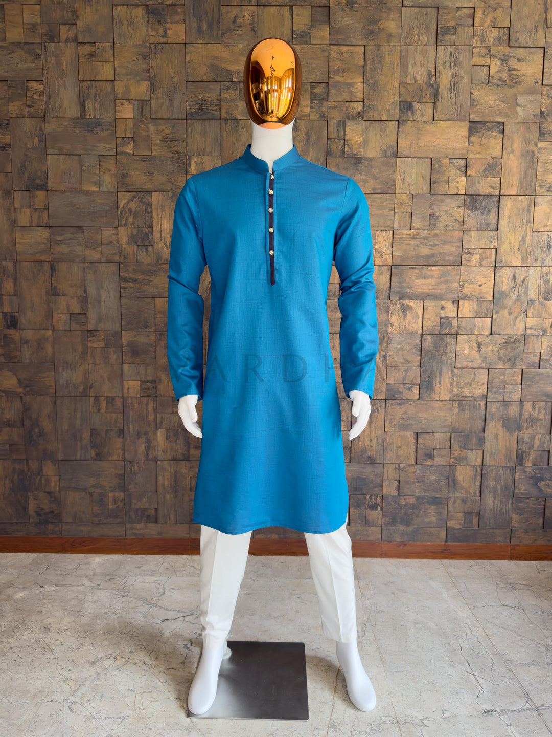 Mannequin wearing a blue kurta against a wooden paneled wall. Front view of a man wearing a House of Vardha peacock blue textured cotton kurta featuring a contrast navy placket. Perfect minimalist men's ethnic wear for festive parties, pujas, and traditional celebrations.