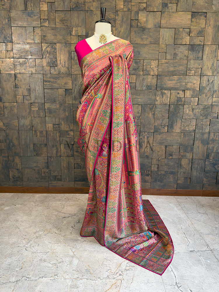 Saree with a pink blouse draped over a mannequin against a wooden paneled wall. Full-length view of a vibrant magenta pink silk saree draped on a mannequin, featuring intricate multi-color Meenakari weaving with traditional figure motifs and heavy borders. Ideal for Indian weddings and grand festive wear.