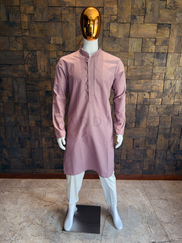 Mannequin wearing a mauve kurta with white pants against a wooden paneled wall. Front view of a man wearing a dusty mauve pink asymmetrical cotton kurta.