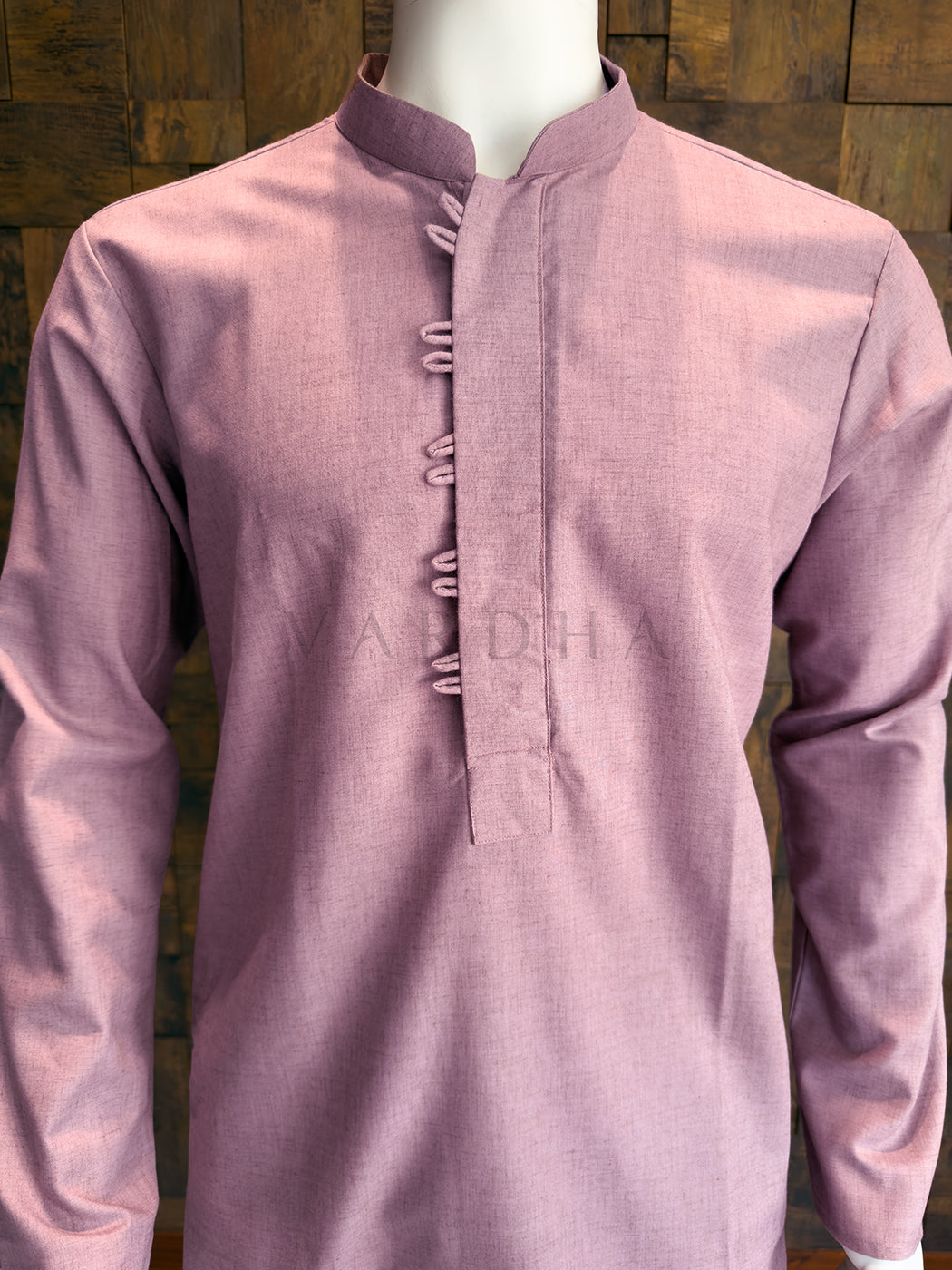 Mauve kurta on a mannequin against a wooden panel background Detailed view of the contrast white double stitching and traditional fabric button loops on the pink kurta.
