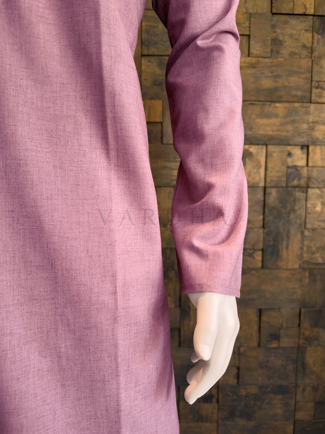 Close-up of a pink shirt sleeve against a wooden paneled background Side profile of the dusty mauve minimalist cotton kurta for men, highlighting the crisp drape.
