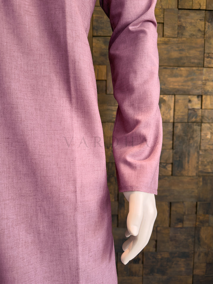 Close-up of a pink shirt sleeve against a wooden paneled background Side profile of the dusty mauve minimalist cotton kurta for men, highlighting the crisp drape.