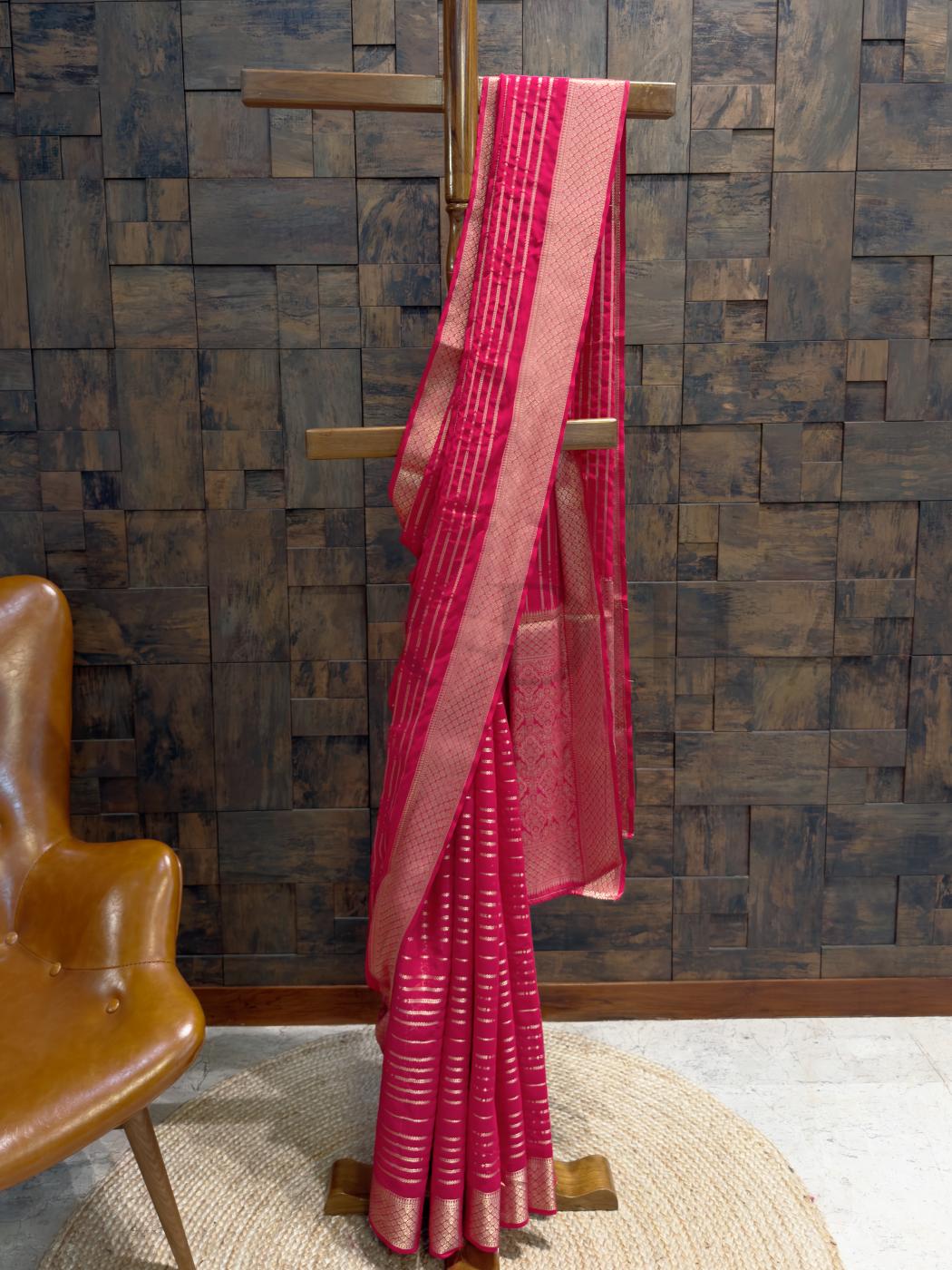 Rani pink feathersoft georgette saree with striped golden zari accents, styled on a wooden hanger for festive elegance., Close-up of zari striped pallu in gold over rich rani pink base with textured weave, ideal for haldi or reception events