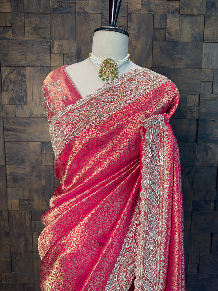 Pink saree with intricate patterns on a mannequin against a wooden paneled wall. Close Up of Scalloped Zircon Stone Border on Rani Pink Silk Saree