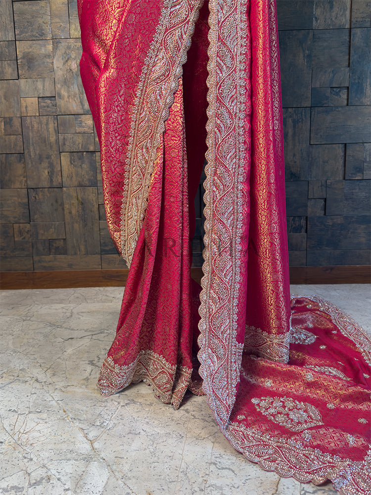 Pink embroidered fabric draped over a wooden surface with a textured wall background. Bottom Drape showing Intricate Cutdana Hand Embroidery on Kanjivaram Fabric