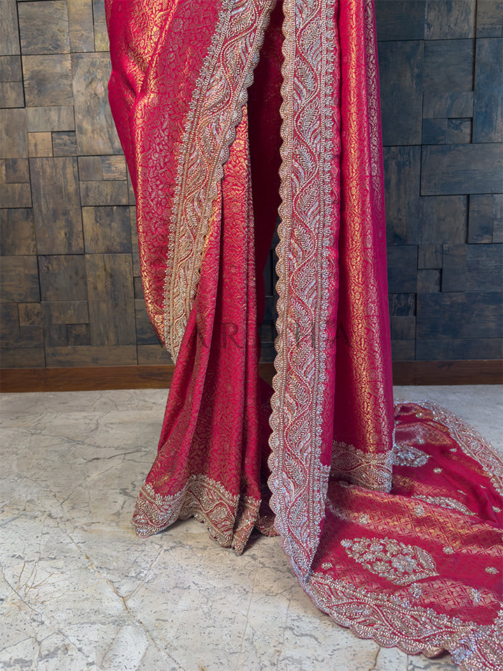 Pink embroidered fabric draped over a wooden surface with a textured wall background. Bottom Drape showing Intricate Cutdana Hand Embroidery on Kanjivaram Fabric