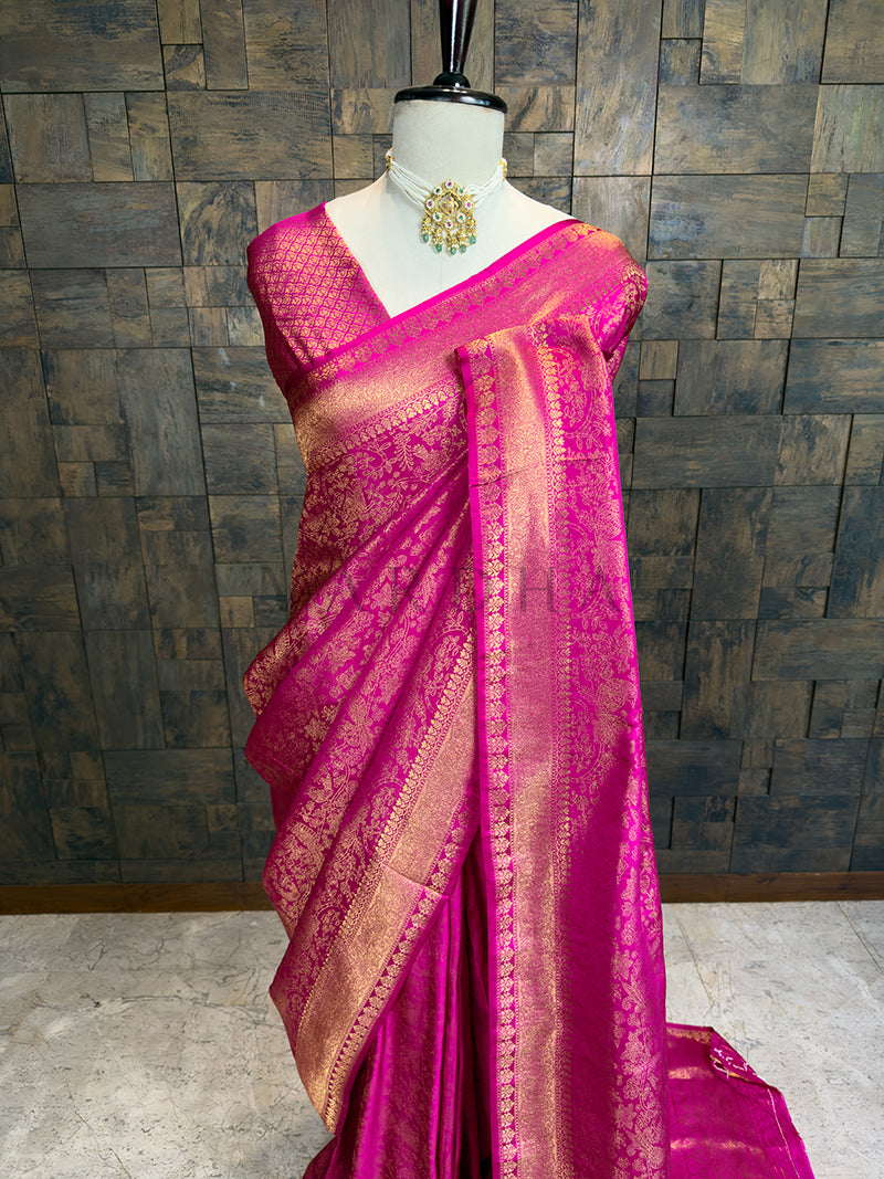Pink saree with gold border on a mannequin against a wooden paneled wall. Elegant Pink Kanjivaram Silk Saree with Zari Weave by House of Vardha showcasing heavy traditional gold brocade craftsmanship. We offer Ready to wear, Pre drape service, Saree Add on, Custom Stitched Blouse, Fall and Edging, Gift Packaging at Complimentary Price!